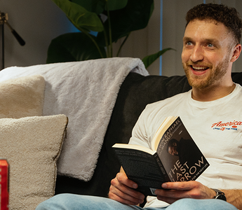 Dayne smiling in his living room sitting on a couch while reading "The Last Arrow" with a Vyper Energy sitting on the table in front of him. 